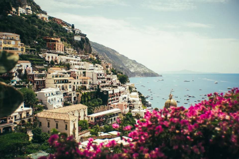 Positano's pastel houses tumbling down the cliffs to the sea, with pink bougainvillea, the tiled church dome and yachts anchored in the bay on the Amalfi Coast