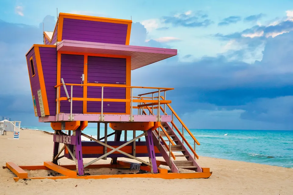A purple and orange lifeguard tower on the sand at Miami Beach, with turquoise Atlantic water and a storm-blue sky behind