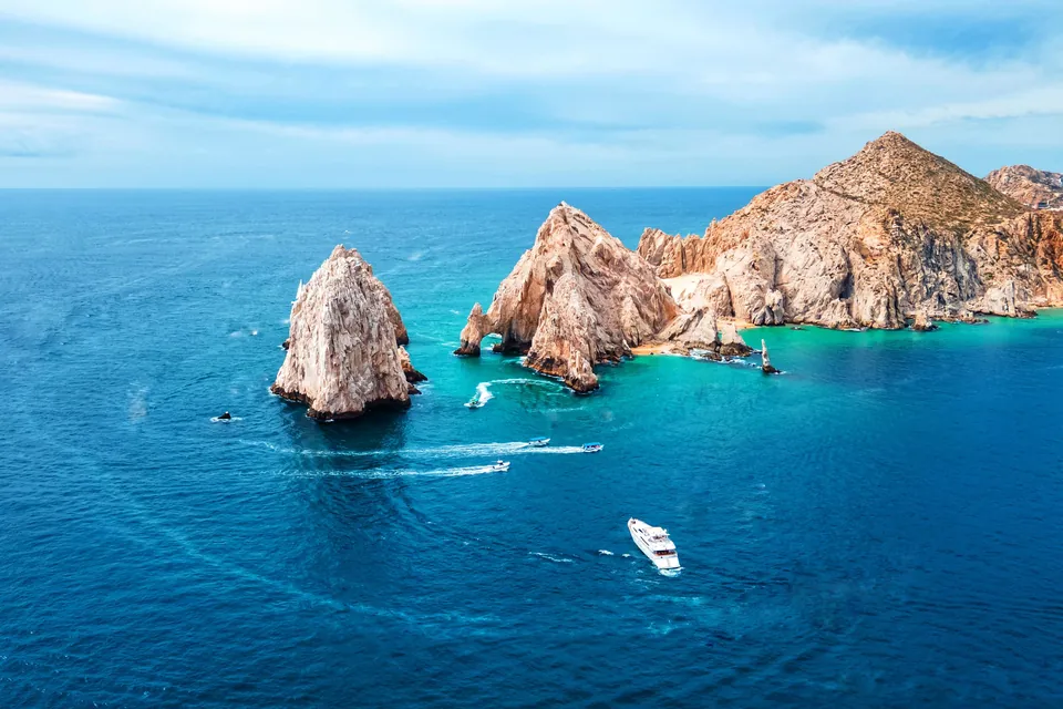 El Arco and the granite sea stacks of Land's End at Cabo San Lucas, with a white yacht cruising through deep-blue water