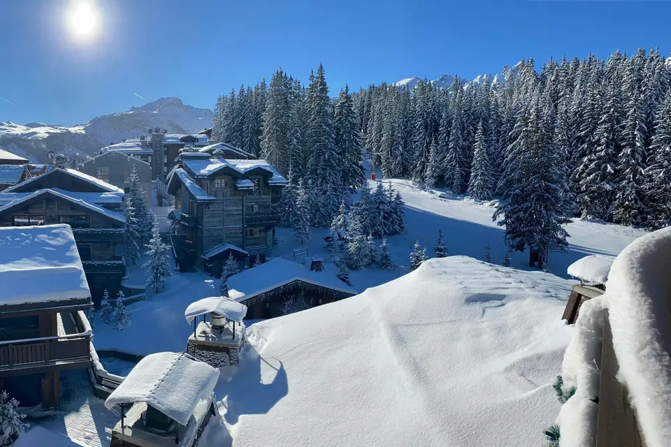 Snow-covered wooden chalets and frosted fir trees beside a groomed piste on a sunny winter day in Courchevel, French Alps