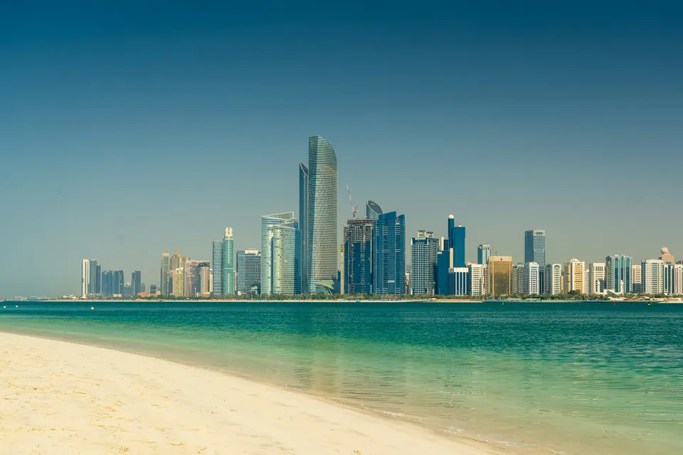 The Abu Dhabi skyline across turquoise water, seen from a white-sand beach on a clear day