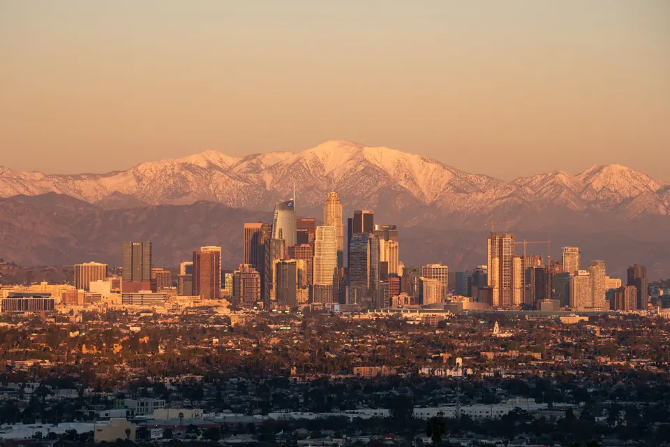 Downtown Los Angeles at golden hour, with the snow-capped San Gabriel Mountains rising behind the skyline