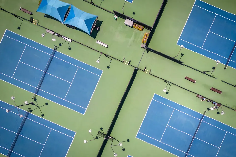 Aerial view of blue hard tennis courts with green surrounds and shade canopies between them