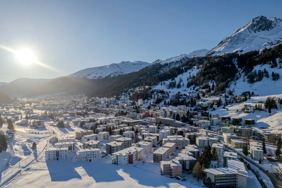 Davos in winter: the snow-covered town spread along the valley floor beneath pine slopes and sunlit Alpine peaks