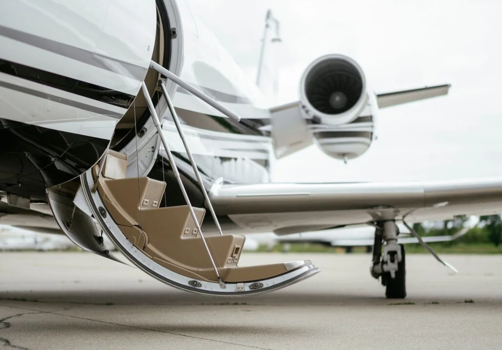 Private jet with stairs extended from the open door, engine visible in the background on the tarmac.